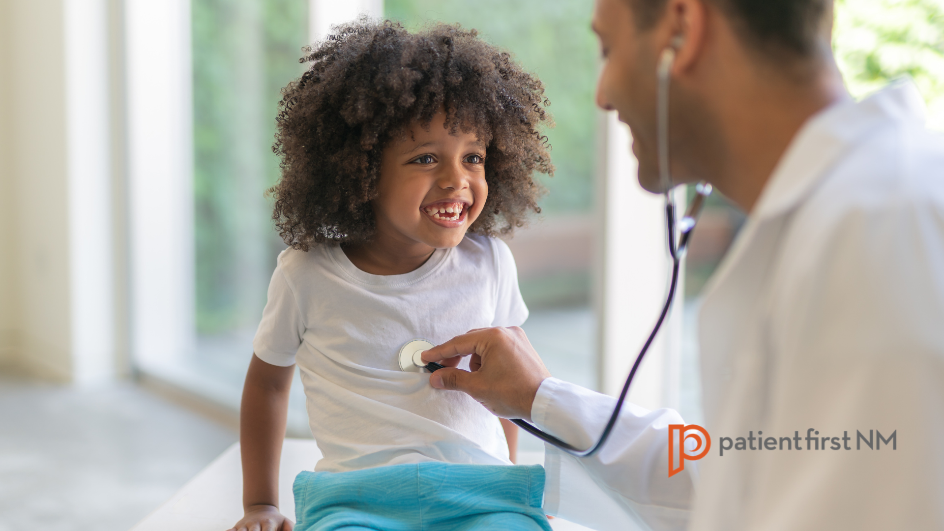 Smiling child being examined with a stethoscope by a doctor during a check-up, with the Patient First NM logo in the corner.
